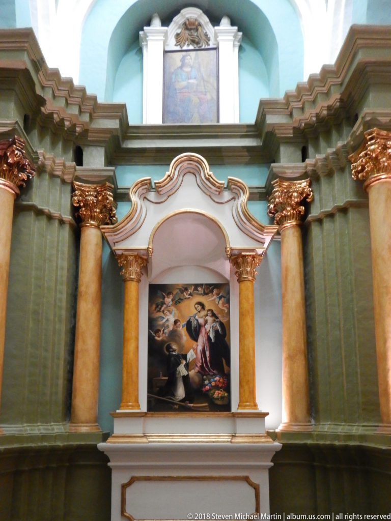 Side altar with paired columns, gilded capitals, curving pediment, green-and-white moldings, and a central religious painting.