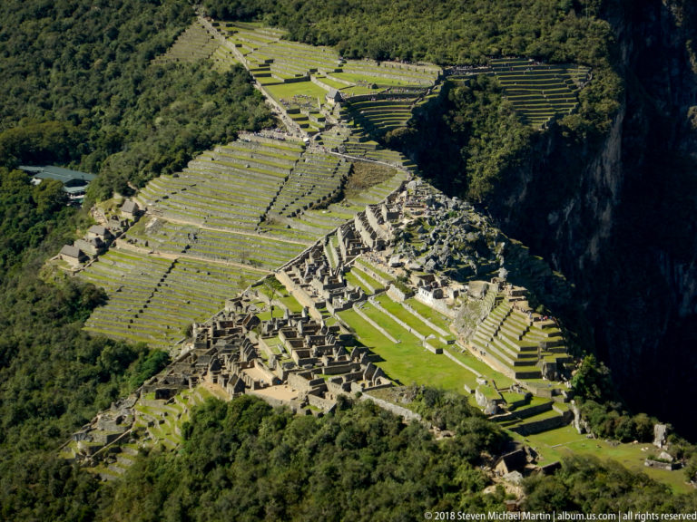 High-angle view from Huayna Picchu over Machu Picchu’s stone complex, open lawns, and extensive terraces.