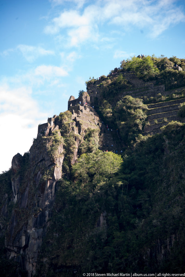 Stone terraces and visitors cross the steep, vegetation-covered upper ridge of Huayna Picchu.