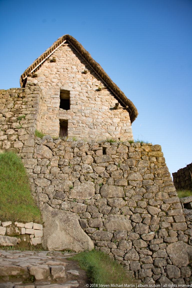 Low-angle view of a stone gable with reconstructed thatched roof and small rectangular openings at Machu Picchu.