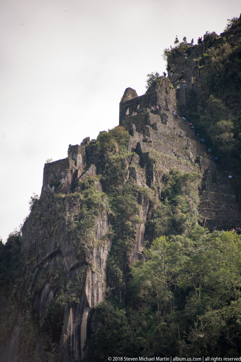 Stone terraces and small masonry structures cling to the steep upper slopes of Huayna Picchu.
