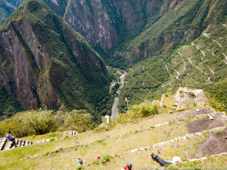 High downward view from the Huayna Picchu route toward a river and switchback road far below.