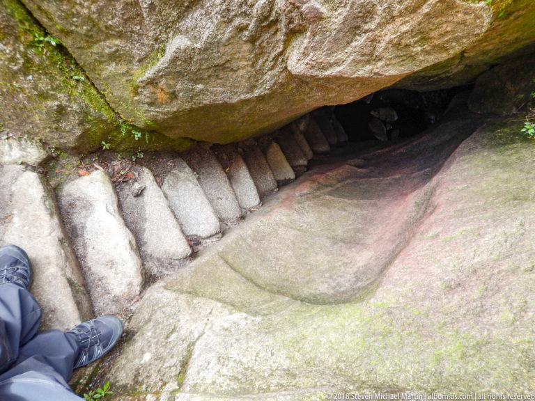 Stone steps pass under a huge overhanging boulder in a narrow section of the Huayna Picchu route.
