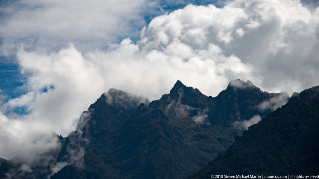 Jagged dark Andean peaks beneath large white clouds and drifting mist near Machu Picchu.