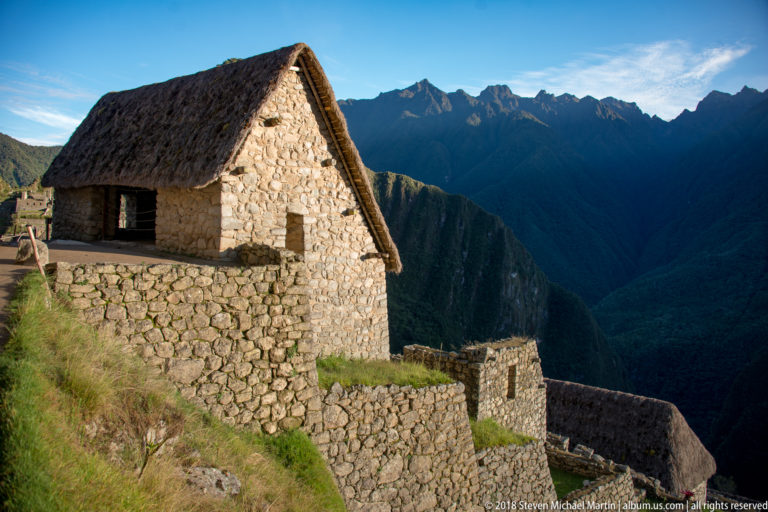 Thatched stone building above stepped retaining walls and a deep mountain valley at Machu Picchu.