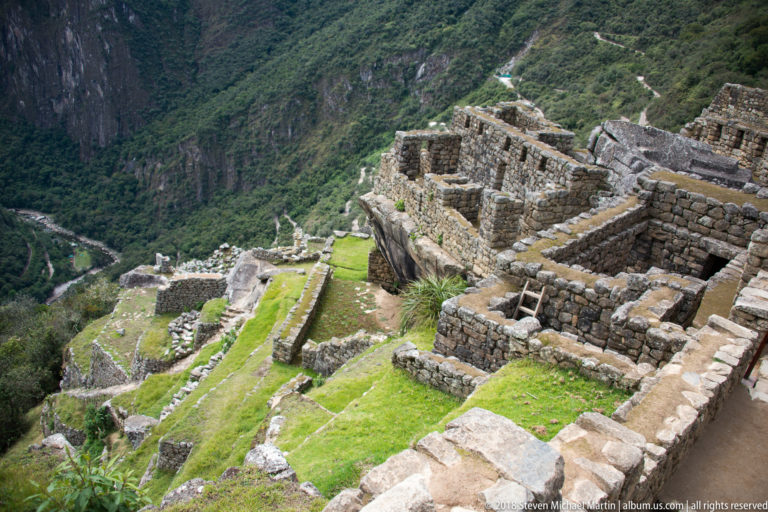 Stone enclosures and green terraces descend toward a deep mountain valley at Machu Picchu.
