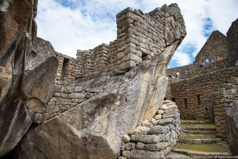 Inca masonry built around a large natural rock outcrop beside a narrow stone stair at Machu Picchu.