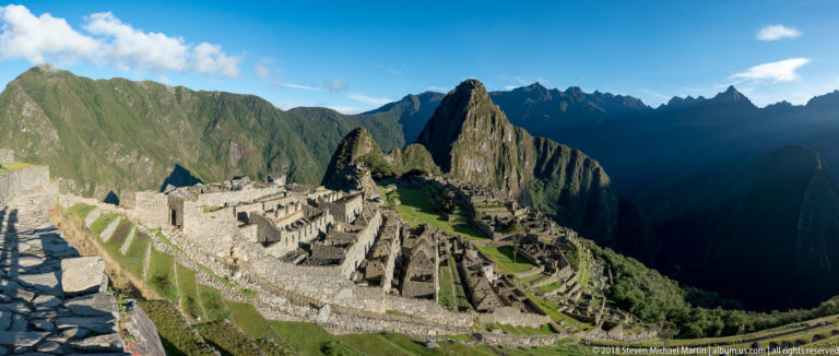 Oblique view across Machu Picchu’s masonry compounds and terraces toward Huayna Picchu and dark mountain ridges.