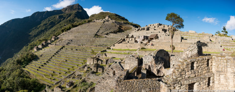 Stone agricultural terraces rise beside roofless Inca buildings on a steep mountainside at Machu Picchu.