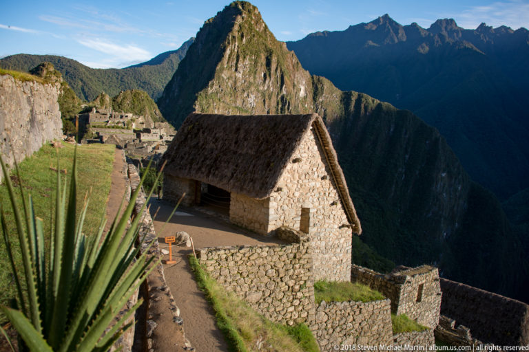 Reconstructed thatched stone building with agave-like plants and Huayna Picchu behind at Machu Picchu.