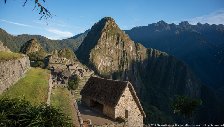 Thatched stone building on an upper Machu Picchu terrace with Huayna Picchu rising behind.
