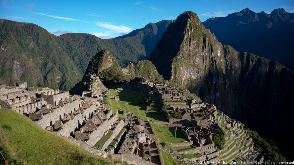 Sunlit Machu Picchu stone compounds and terraces below the steep peak of Huayna Picchu.