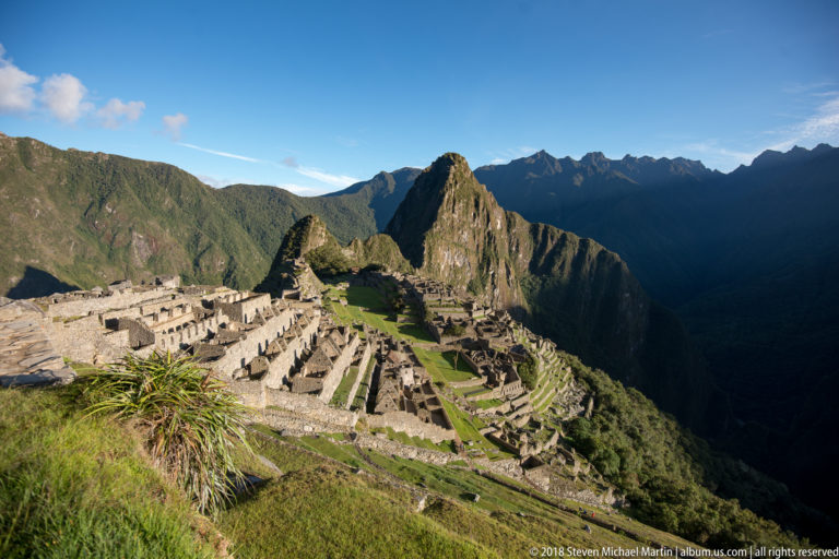Late-afternoon view of Machu Picchu’s masonry and terraces beneath Huayna Picchu and distant mountains.
