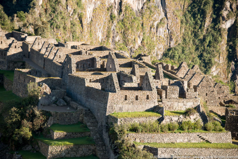 Compact cluster of gabled stone structures above green terraces at Machu Picchu.