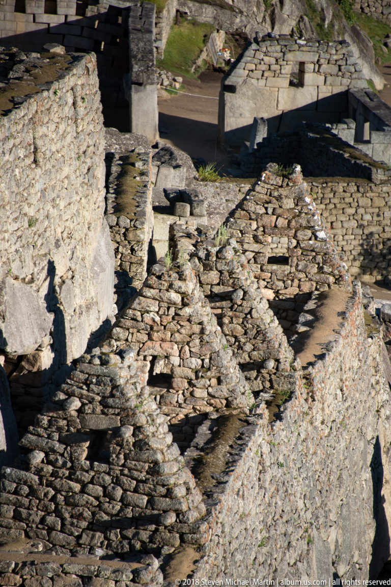 High-angle detail of roofless stone rooms and narrow passages at Machu Picchu.