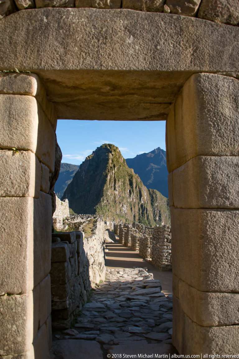 Finely fitted rectangular stone doorway framing a sunlit path and rounded mountain at Machu Picchu.