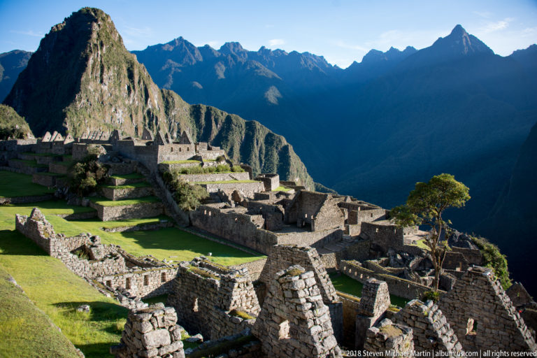 Layered stone compounds and green lawns at Machu Picchu beneath Huayna Picchu and jagged mountains.
