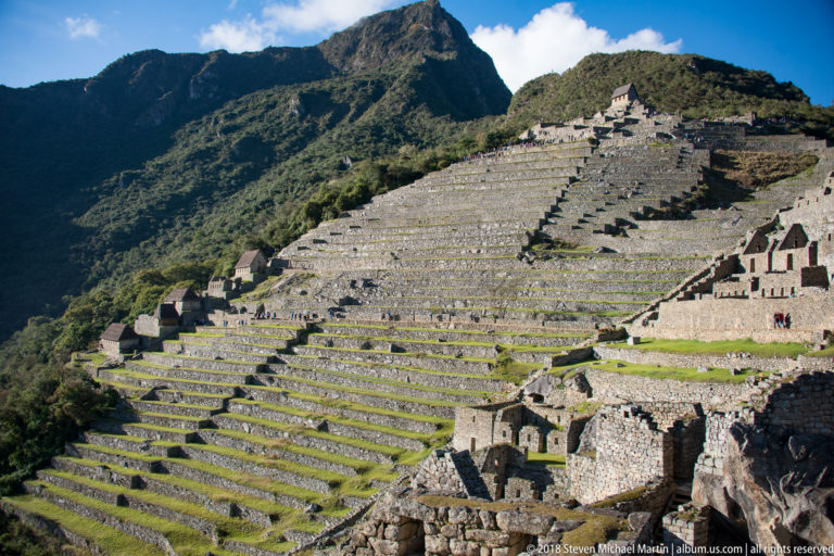 Broad stepped terraces rise toward upper stone structures at Machu Picchu beneath steep mountains.