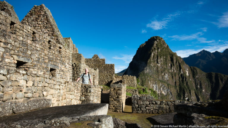 Stone walls and a narrow doorway at Machu Picchu frame Huayna Picchu beneath a vivid blue sky.