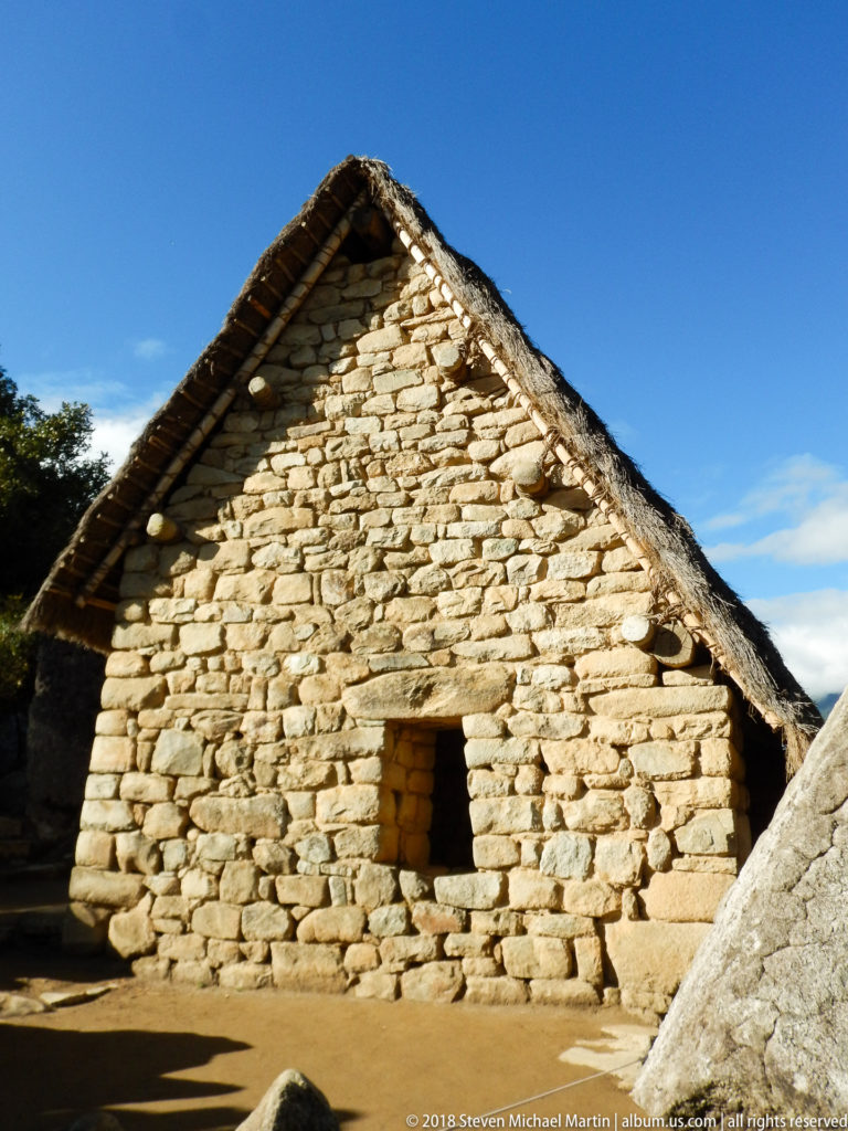 Front view of a stone building with a reconstructed thatched gable roof and small trapezoidal opening at Machu Picchu.