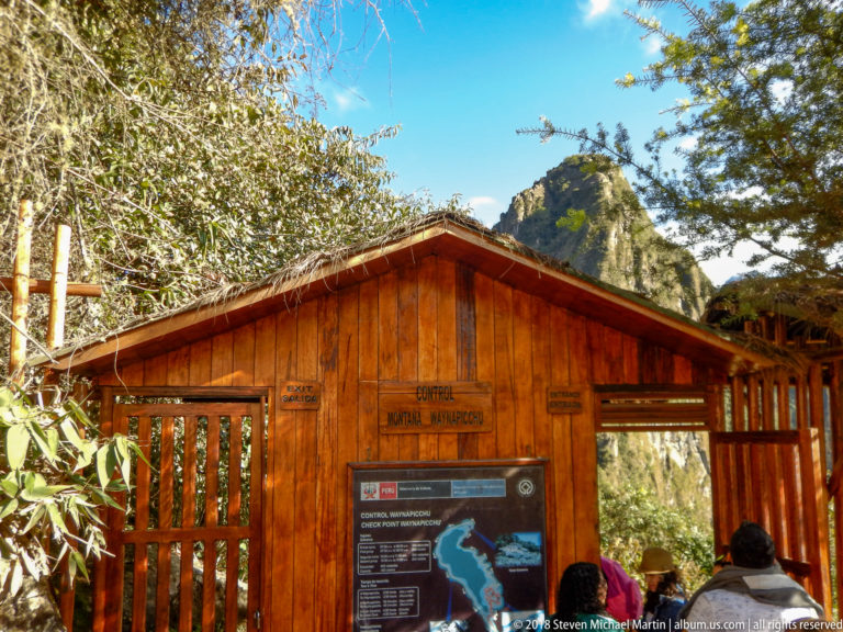 Wooden Huayna Picchu trail control building with posted information and visitors at the entrance.