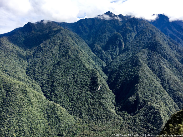 Forested Andean ridges descend into deep valleys beneath cloud-touched peaks near Machu Picchu.