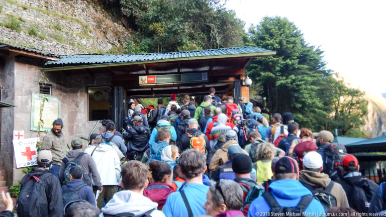 Large crowd of visitors with backpacks waiting at a roofed access point near Machu Picchu.