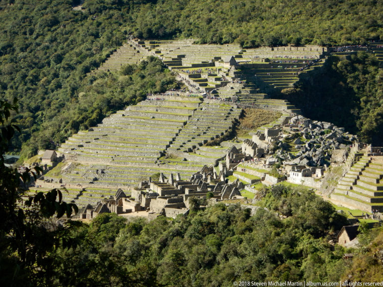 Wide elevated view of Machu Picchu’s extensive terraces with roofless stone buildings clustered at lower right.