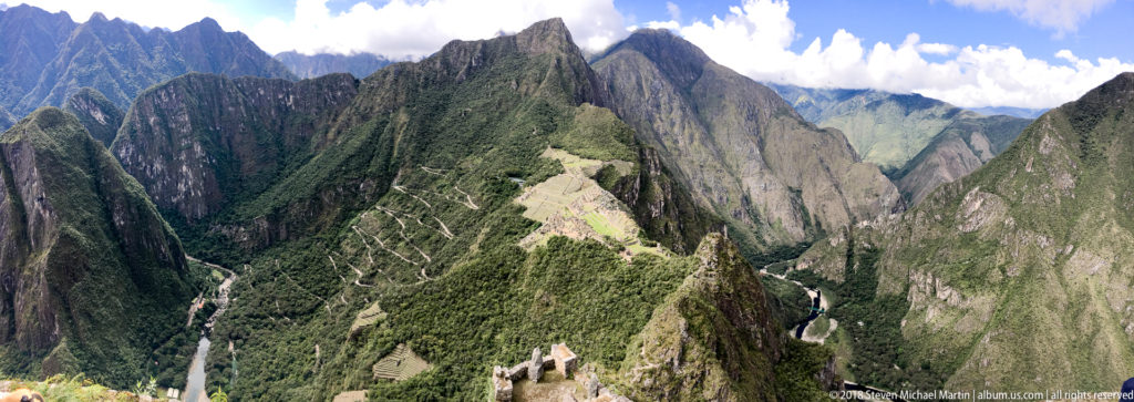 High view from Huayna Picchu across jagged Andean peaks to Machu Picchu centered on the ridge below.