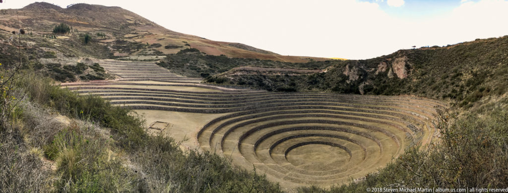 Wide view of Moray's concentric bowl, parallel hillside terraces, rectangular ground outline, and enclosing rocky slopes.