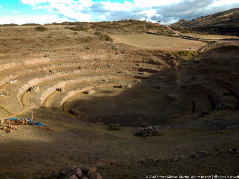 Partly shadowed circular terraces at Moray, with sunlit upper rings, dark lower benches, and scattered stone piles.