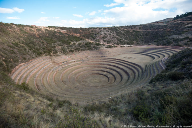High establishing view of Moray's concentric terraced depression enclosed by scrub-covered hills and highland paths.