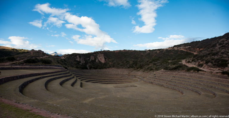 Wide terraced bowl at Moray with concentric stone-edged benches descending toward a broad floor beneath a blue sky.