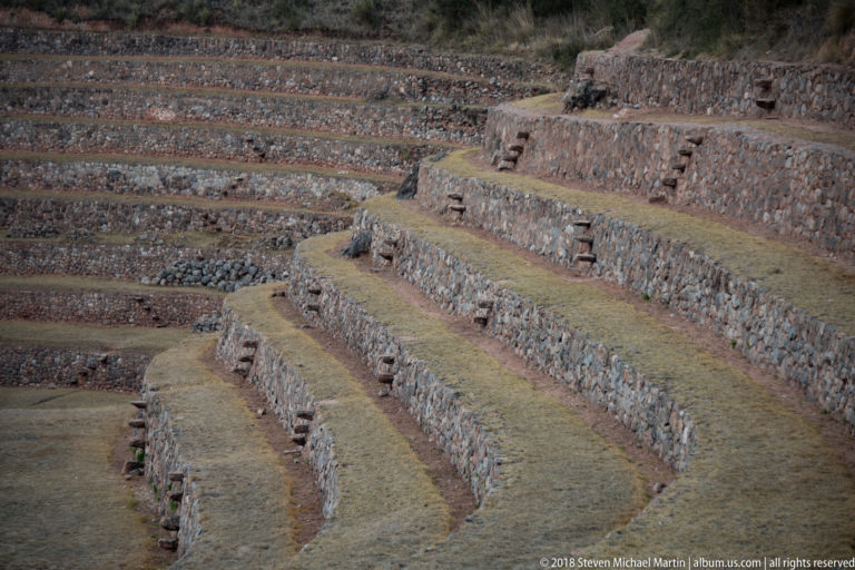 Closely framed curved terraces at Moray with stacked stone walls, narrow grassed benches, and projecting-stone steps.