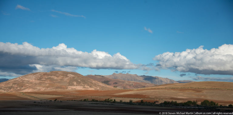 Rolling brown and rust-colored Andean uplands under a deep blue sky with a long bank of white clouds.