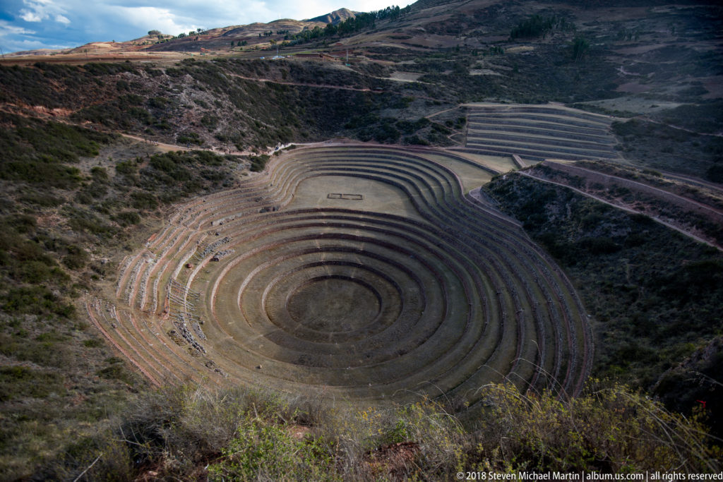 High oblique view of Moray's deep concentric terrace bowl, with a rectangular ground feature and hillside terraces beyond.