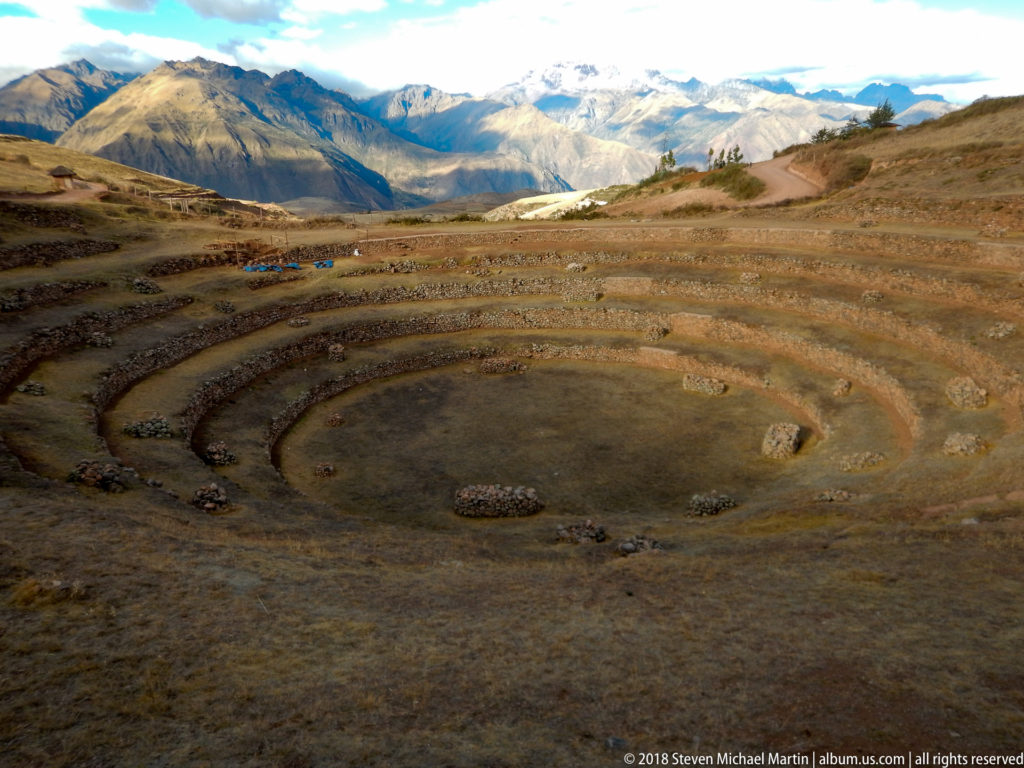 Shallow concentric terraces at Moray in the foreground with pale layered Andean mountains beyond.