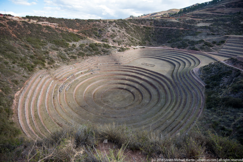 High overview of Moray's concentric terraced bowl with straighter terraces climbing the upper right hillside.