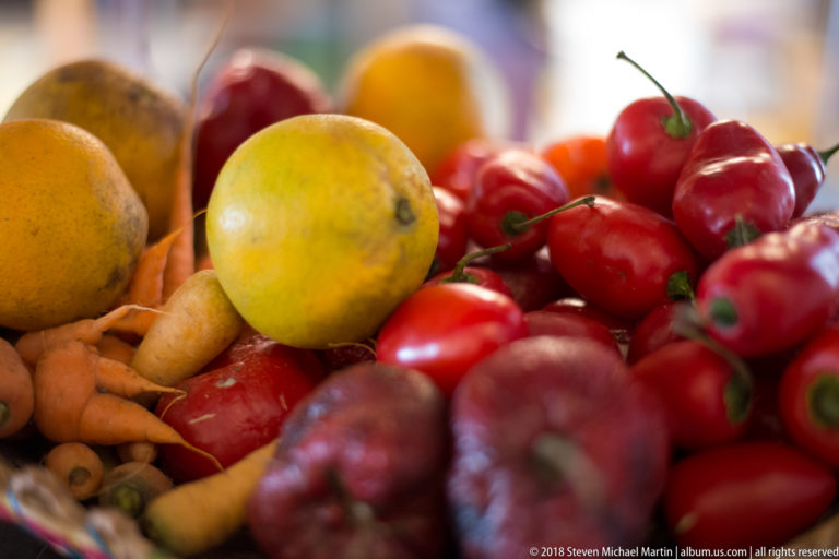 Basket filled with yellow citrus, red peppers, red onions, and pale root vegetables.