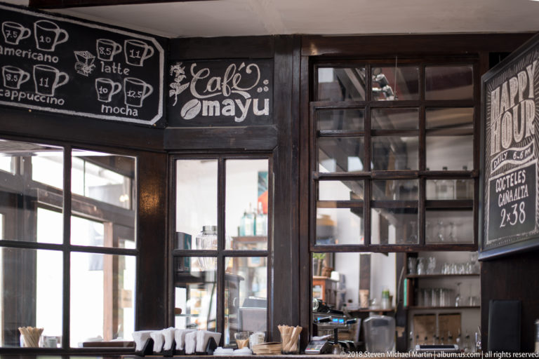 Interior of Café Mayu with chalkboard lettering, dark wooden windows, counters, and dining tables.