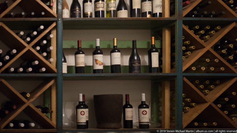 Wine bottles arranged on central shelves and diagonal wooden storage racks in a dark interior.