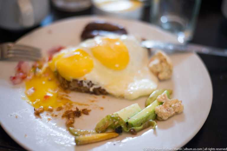 Two sunny-side-up eggs on a savory base with small portions of cooked vegetables on a white plate.