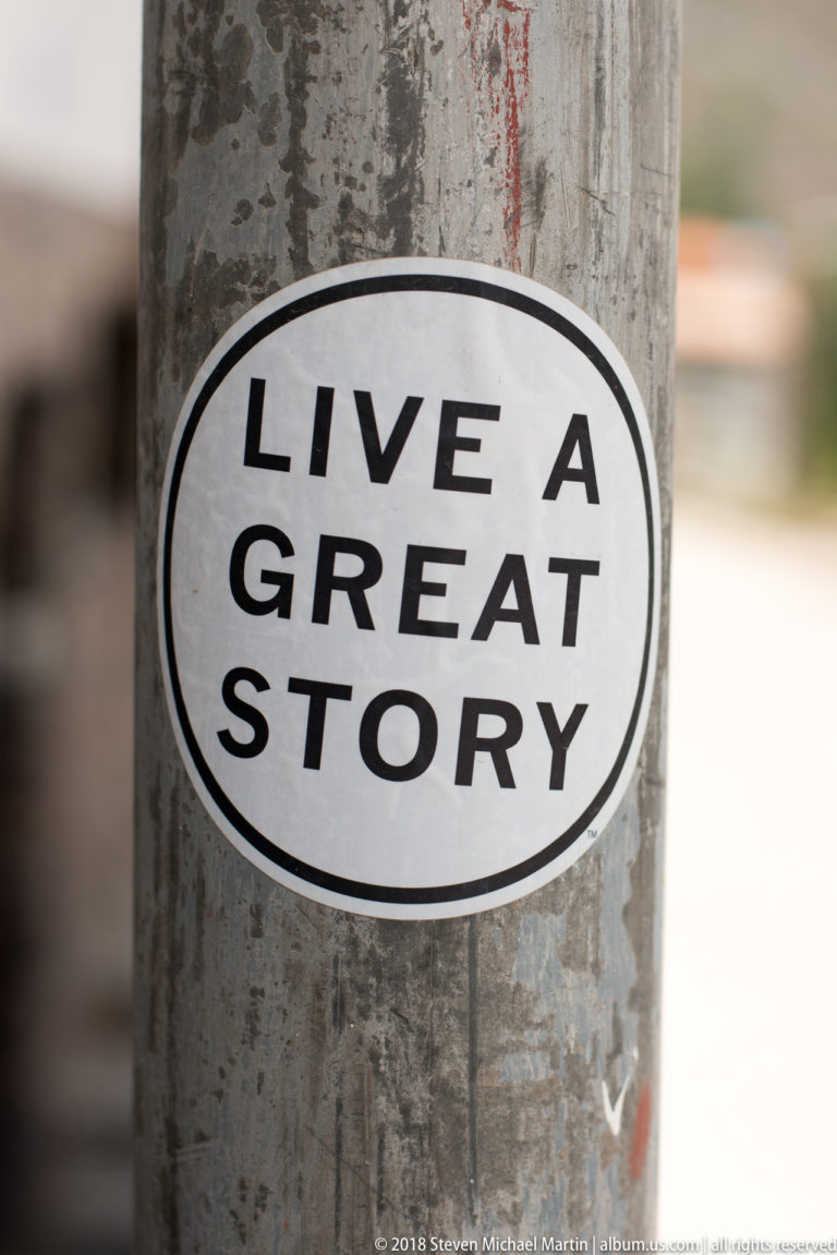 Sticker reading “LIVE A GREAT STORY” attached to a weathered pole in Ollantaytambo.