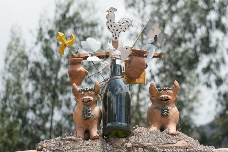 Rooftop ornament with two ceramic bulls, a rooster, vessels, metal crosses, and a dark bottle.