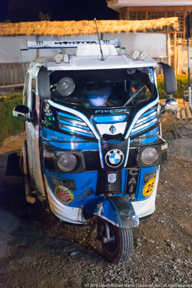Front view of a decorated blue-and-white mototaxi with chrome trim, stickers, and auxiliary lights.