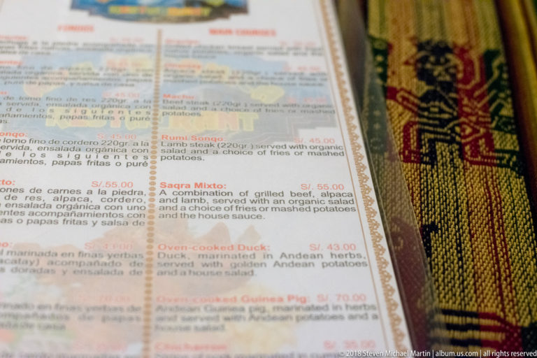 Close-up of a bilingual restaurant menu listing grilled meats, duck, and oven-cooked guinea pig.