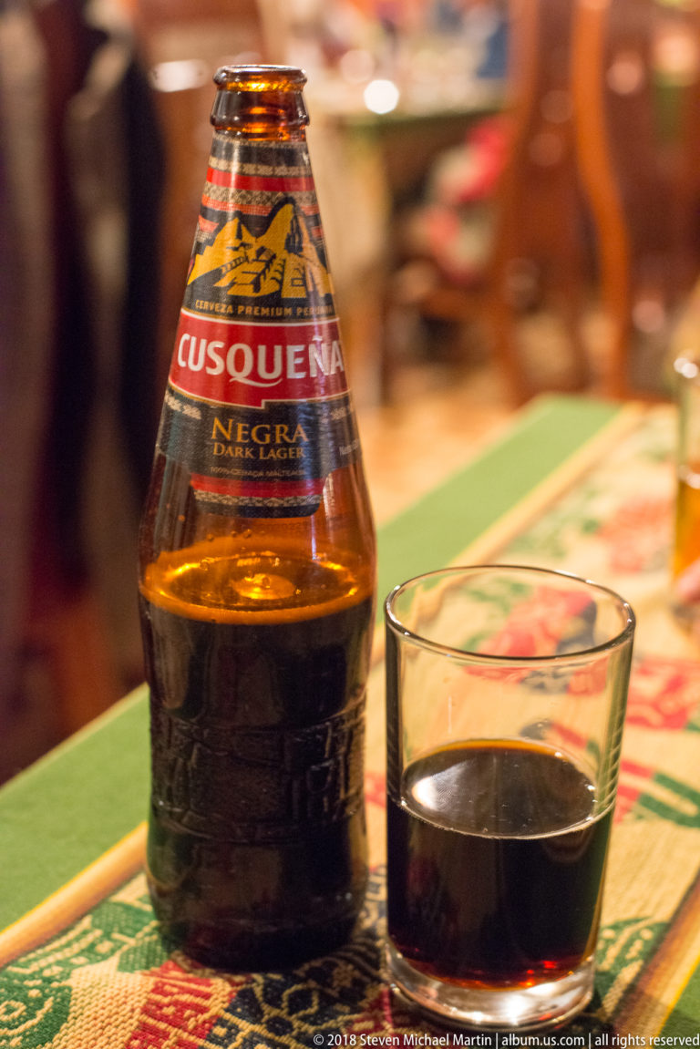 Close view of a Cusqueña Negra beer bottle beside a small glass of dark beer.