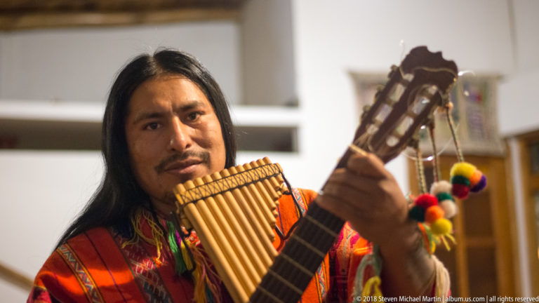 Close portrait of an Andean musician holding panpipes beside the neck of a guitar.