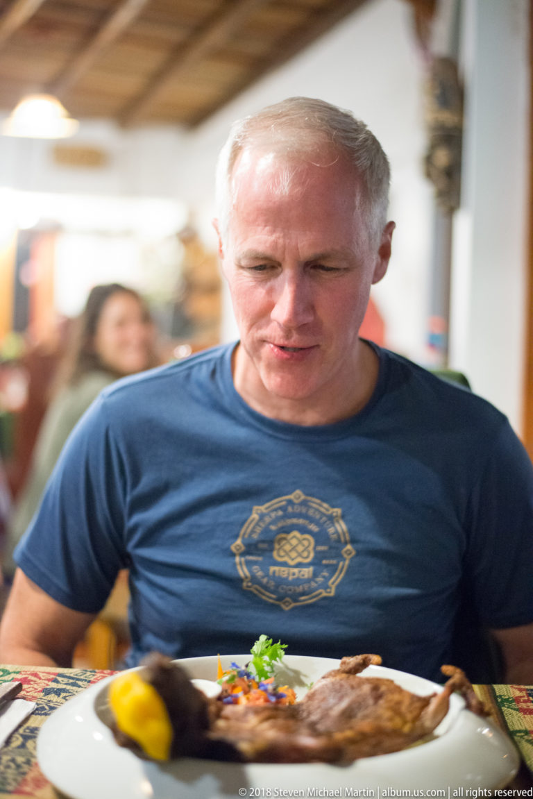 Man seated at a restaurant table behind a plate of roasted guinea pig.