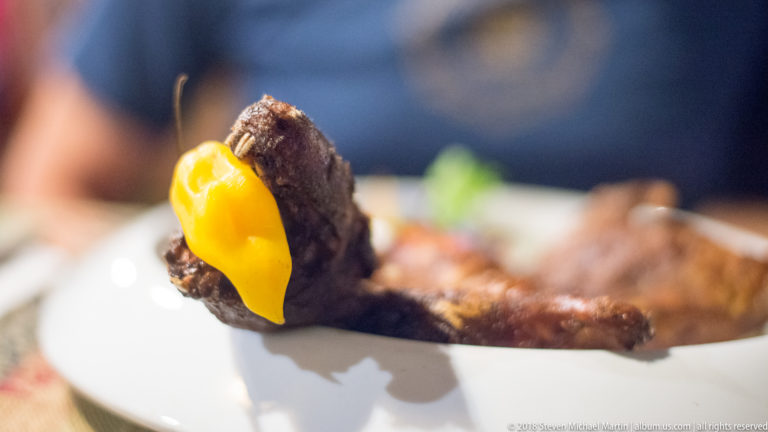 Roasted guinea pig head with yellow pepper garnish, shown in close-up above the rest of the plate.